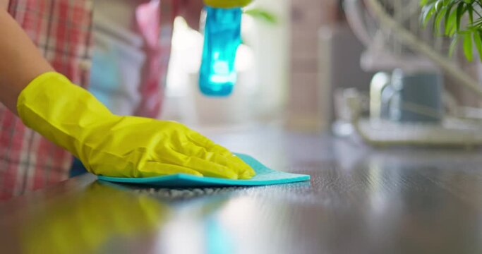 Housewife in yellow rubber gloves wiping wooden table surface in kitchen at home