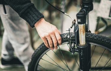 A young man holds a bicycle wheel with his hand.