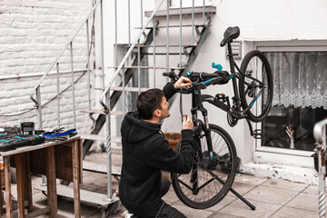 A young man is repairing a bicycle in the backyard of the house.