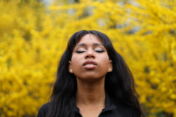 Relaxed african woman meditates and breathes fresh air against the backdrop of yellow vegetation.