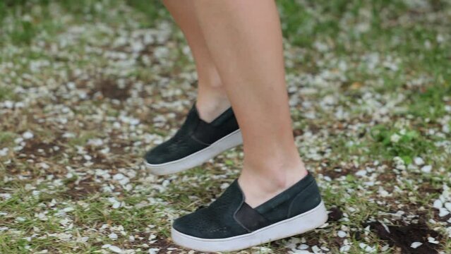 the feet of a girl running through grass covered in white petals from a blooming apple tree in the orchard. 