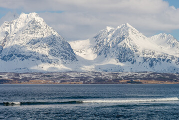 Surfing waves in front of some snowy pointy peaks