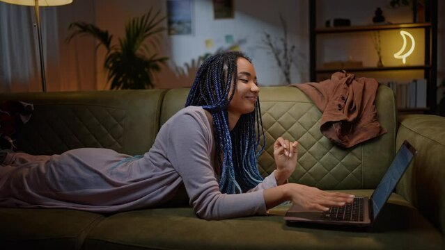 African American young woman closing laptop lid while finishing her graduation work, lying on sofa