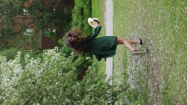 young brunette girl in a green dress runs against the background of a blooming apple tree. vertical video