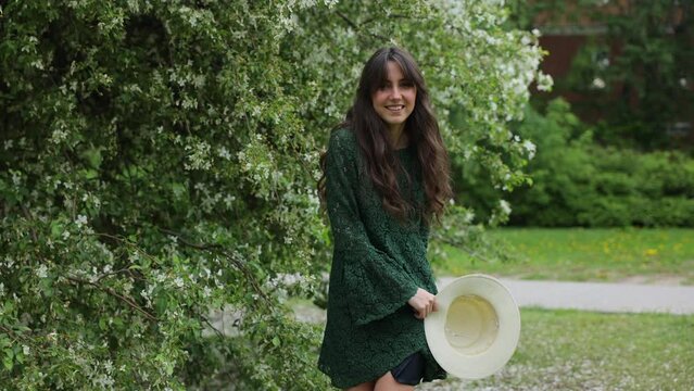 A young brunette girl in a green dress walking in front of a blooming apple tree in the city. Urban Parks and Recreation 