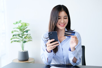 Smiling asian woman capable ebanking app user hold credit card smartphone satisfied with easy quick safe way to pay. Positive young lady sit on couch check bank account balance provide distant payment