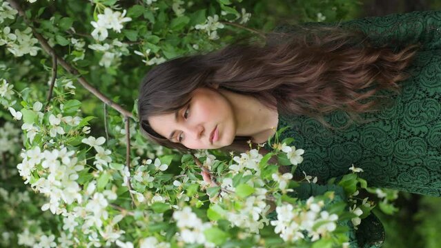 Portrait of a beautiful young girl in an Apple blossom garden. Vertical video