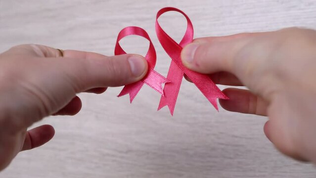 Female Hands Show Two Pink Ribbons on a Wooden White Background. Close up. Hand with a breast cancer symbol. Cancer information. Hope. October month. International AIDS, Cancer Day. Disease awareness.