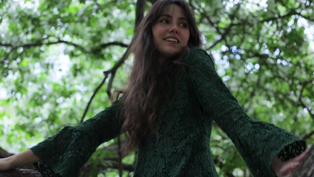 A young woman is sitting on a branch of a blossom apple tree in the forest. Vertical video