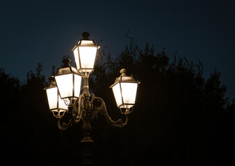 Farola iluminada de estilo clásico en Castro, Italia. Silueta de la estructura de la farola y los...