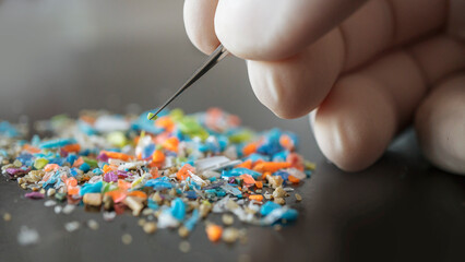 Macro shot of a person with medical gloves and tweezers inspecting a pile of micro plastics....