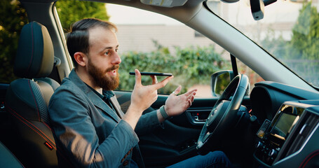 Businessman recording voice message to cellphone in modern car. Focused male professional recording voice message on phone in automobile.