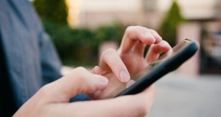 Close up. Caucasian man hands using mobile phone while standing on street. Male tapping and texting on mobile phone. Outdoors.