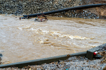 Construction equiment under fast moving water along a rocky embankment.