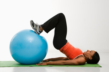 Profile of African American woman stretching on mat with feet on exercise ball.