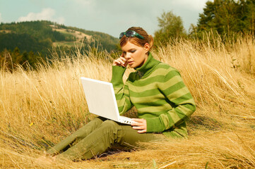 Naklejka na ściany i meble Young business woman working on laptop computer on golden meadow at mountains outdoors