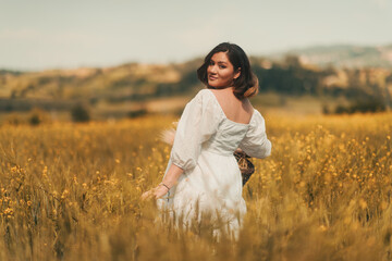 A pregnant woman in a white dress carries a basket of dry flowers in a golden wheat field, embodying the spirit of Mother's Day