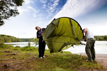 A couple setting up a tent in the forest by a lake © Designpics