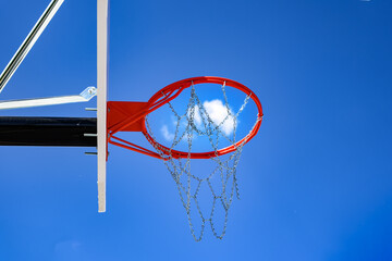 A new basketball backboard with a new hoop and metal netting has a beautiful blue sky with white puffy clouds in the background.  Looking up at basketball net outdoors in Windsor in Upstate NY.