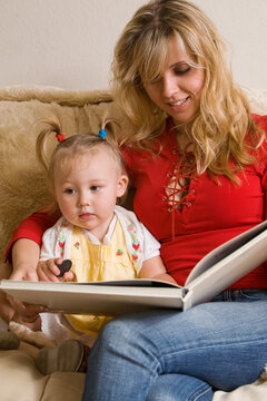 Portrait of an attractive young mother and an adorable blond toddler sitting on sofa reading a book
