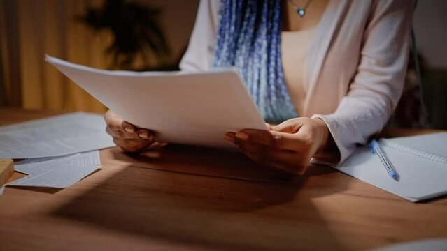 Close-up of a woman's hands flipping through sheets of paper while sitting at a desk