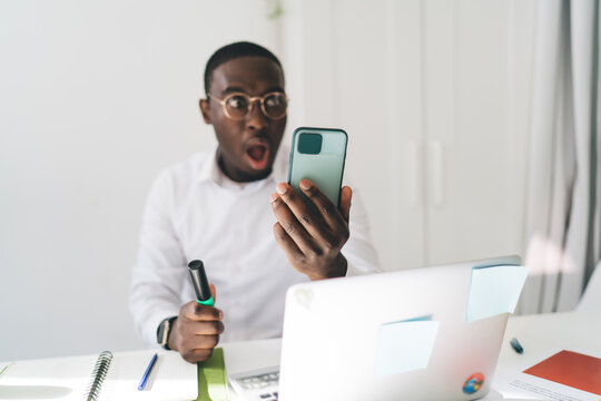Shocked black man looking at screen of smartphone in office