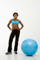 African American young adult woman smiling at viewer with hands on hips next to exercise ball.