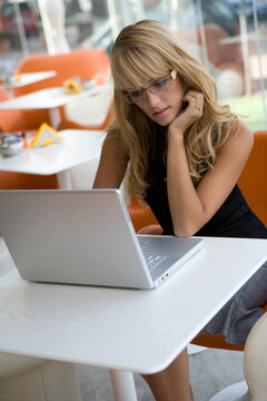 Attractive blonde young woman working with a laptop sitting at a cafe table wearing eyeglasses