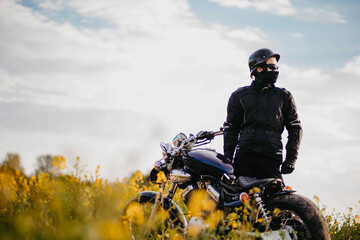 male motorcyclist in motorcycle outfit with custom bobber motorcycle in a field of flowers.