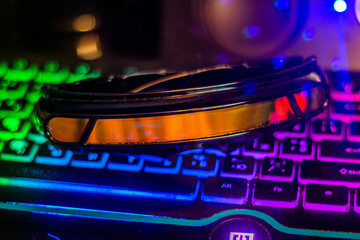 Black futuristic glasses with orange glass lie on a multi-colored keyboard	
