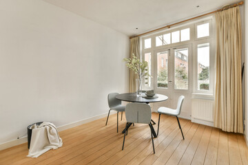a living room with wood flooring and white walls, there is a small round dining table in front of the window