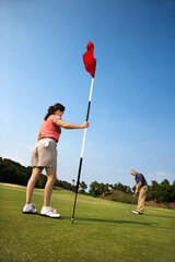 Caucasion mid-adult man putting golfball while Caucasion mid-adult woman holds flag.