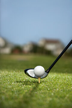 Image of golf ball on tee with golf club behind ball.