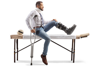 Profile shot of an injured man with an orthopedic boot and arm sling sitting on a therapy table