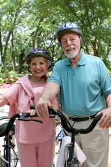An attractive senior couple bicycling with helmets on.