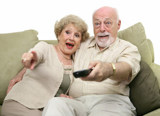 A senior couple really enjoying a television program.  White background.
