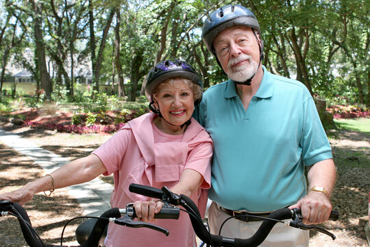 An attractive senior couple bicycling together wearing helmets.