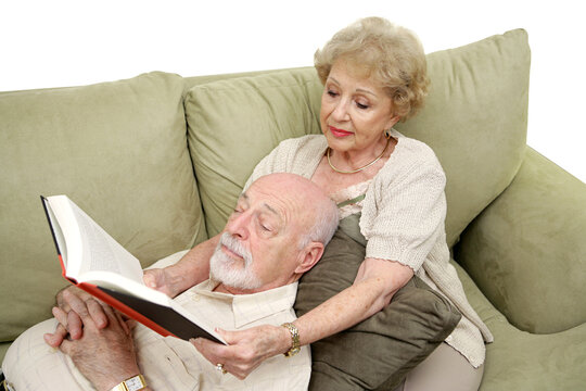 A senior man taking an afternoon nap while his wife reads to him.  White Background.