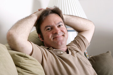 A handsome, friendly man relaxing at home with his hands behind his head.