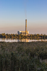 Obraz premium A waste processing plant at the lake sunset, with smoking chimneys. Energy's generated but it results in environmental and air pollution.