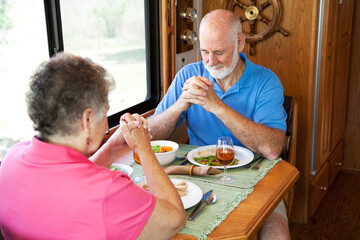 Senior couple say a prayer of thanksgiving over a turkey dinner in their motor home.
