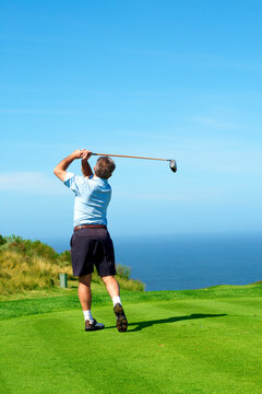 Senior male golfer playing golf from the tee box facing the ocean on a beautiful summer day