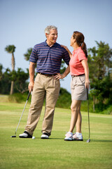 Caucasion mid-adult man and woman standing on golf course talking to each other.