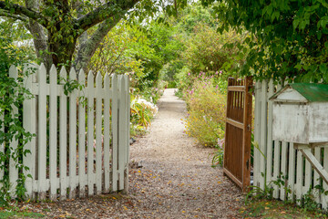 Gravel path leading between tow open gated through old English style garden