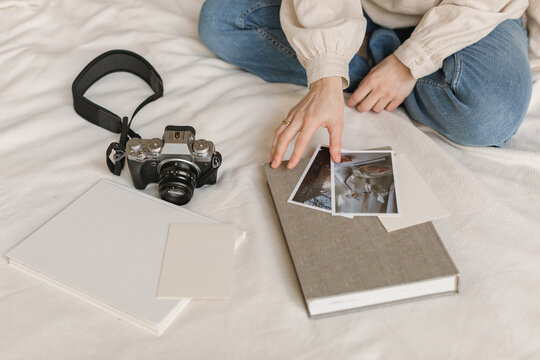 Woman sitting on a bed with a digital camera looking at printed photos