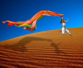 Beautiful woman jumoping over the sand dunes with a colored scarf