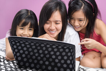 Asian mother and daughters playing with laptop in the bedroom