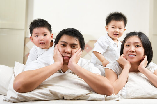 Asian family pose on bed with two kids