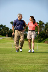 Obraz premium Caucasion mid-adult man and woman walking on golf course talking to each other.