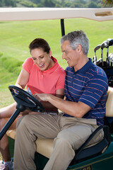 Fototapeta premium Mid-adult male and female in golf cart pointing at score card.
